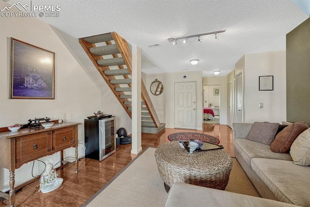 living room with a textured ceiling, wine cooler, wood finished floors, visible vents, and stairs