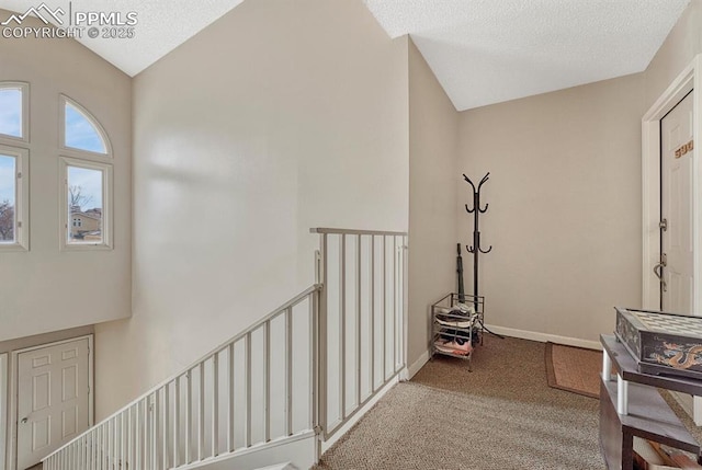 hallway featuring a textured ceiling, an upstairs landing, baseboards, vaulted ceiling, and carpet