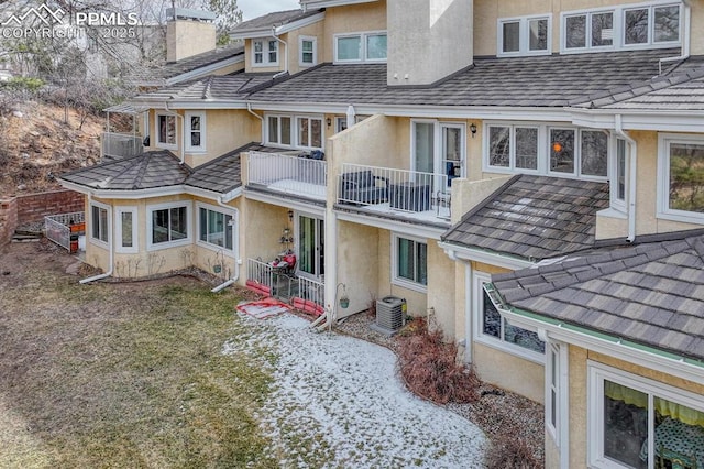 back of house featuring cooling unit, a chimney, a balcony, and stucco siding