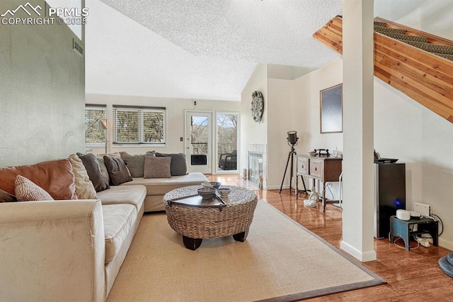 living room with baseboards, visible vents, lofted ceiling, wood finished floors, and a textured ceiling