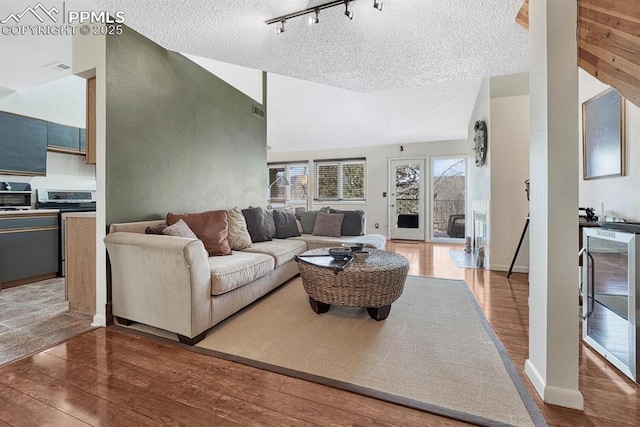 living area featuring lofted ceiling, a textured ceiling, track lighting, wood finished floors, and beverage cooler