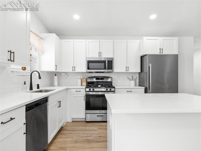 kitchen with appliances with stainless steel finishes, tasteful backsplash, light wood-type flooring, white cabinets, and sink