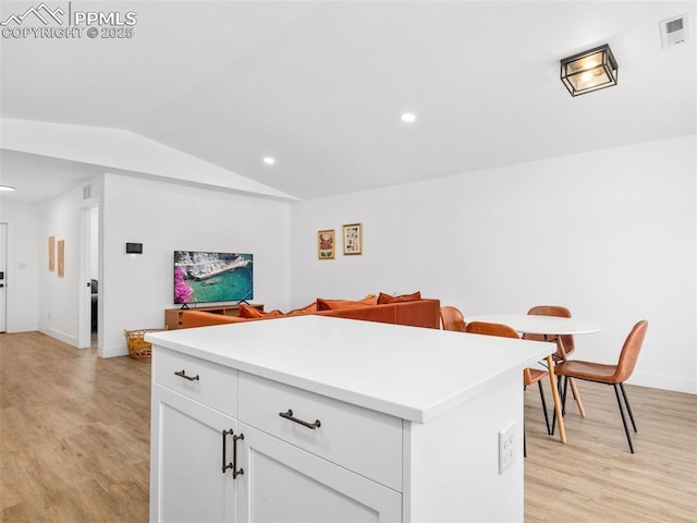 kitchen with white cabinets, vaulted ceiling, a kitchen island, and light hardwood / wood-style flooring