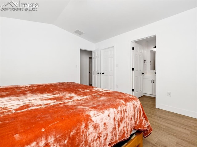 bedroom with vaulted ceiling, hardwood / wood-style floors, and connected bathroom