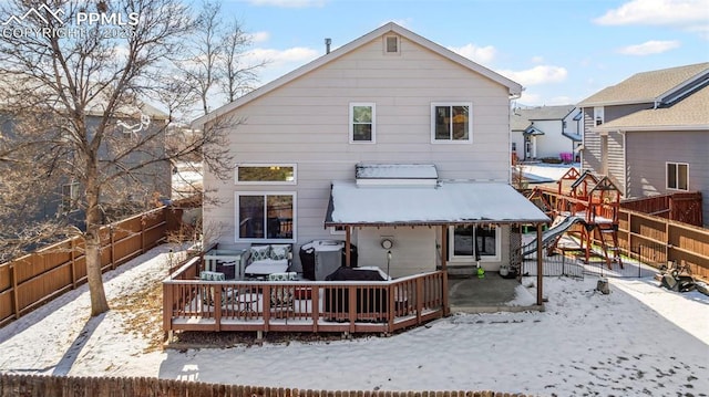 snow covered back of property with a playground and a deck