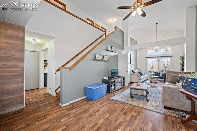 living room with dark wood-type flooring, ceiling fan with notable chandelier, and high vaulted ceiling