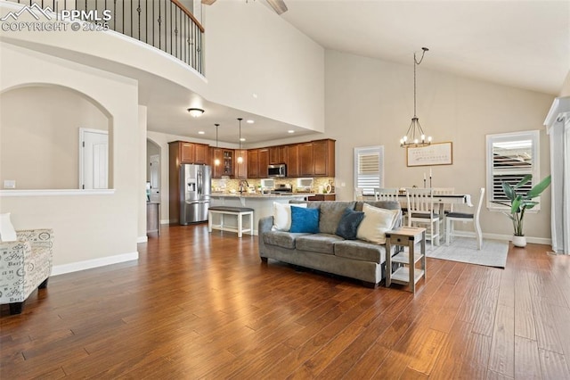 living area with baseboards, dark wood-style flooring, an inviting chandelier, high vaulted ceiling, and recessed lighting