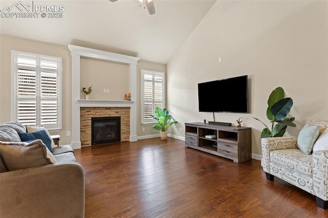 living area with a ceiling fan, a stone fireplace, baseboards, and wood finished floors