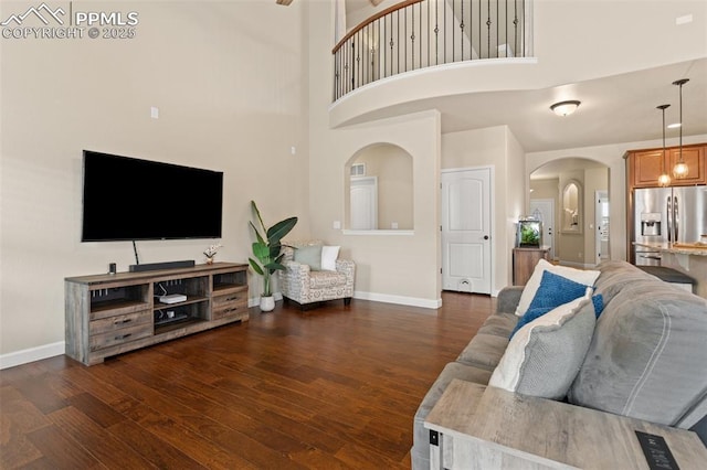 living room with a towering ceiling, baseboards, arched walkways, and wood finished floors