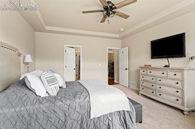 bedroom featuring light carpet, visible vents, baseboards, ceiling fan, and a tray ceiling