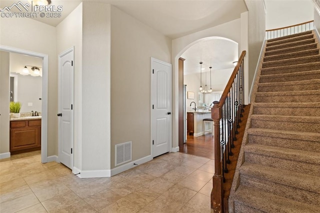 foyer entrance with baseboards, visible vents, arched walkways, stairway, and an inviting chandelier