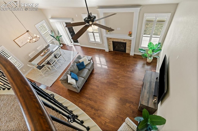 living area with a stone fireplace, plenty of natural light, wood finished floors, and baseboards