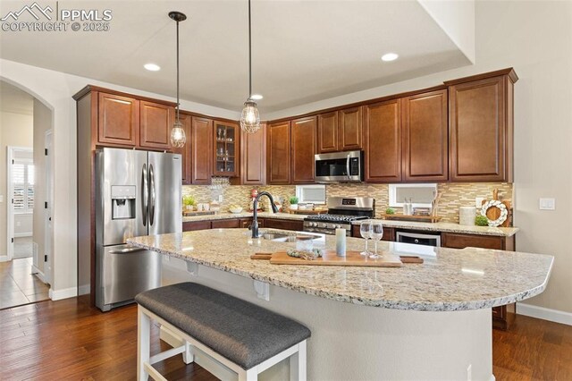 kitchen with appliances with stainless steel finishes, arched walkways, a sink, and tasteful backsplash