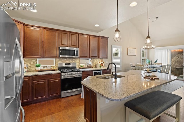 kitchen featuring lofted ceiling, a sink, appliances with stainless steel finishes, light stone countertops, and dark wood-style floors