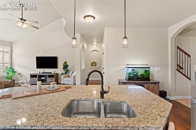 kitchen featuring arched walkways, a sink, open floor plan, dark wood-style floors, and decorative light fixtures