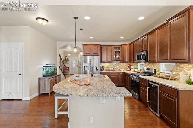 kitchen with arched walkways, wine cooler, stainless steel appliances, a sink, and a kitchen bar