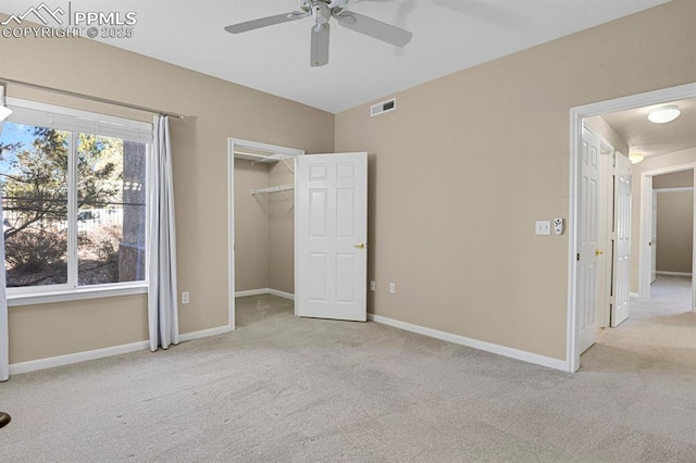 unfurnished bedroom with a walk in closet, light colored carpet, a closet, and ceiling fan