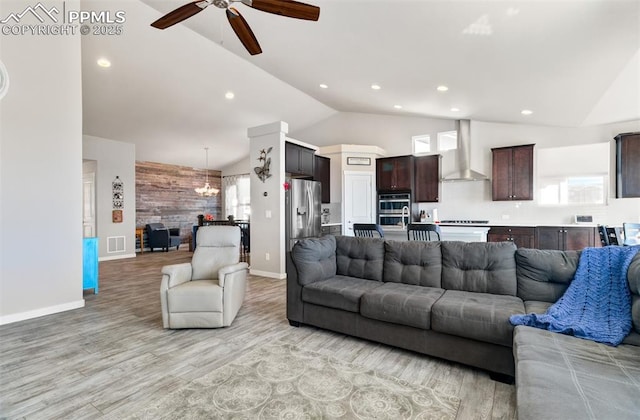 living room featuring ceiling fan with notable chandelier, high vaulted ceiling, wooden walls, and light hardwood / wood-style floors