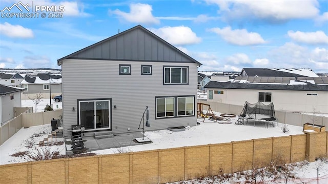 snow covered rear of property with a patio, a fenced backyard, a trampoline, cooling unit, and board and batten siding