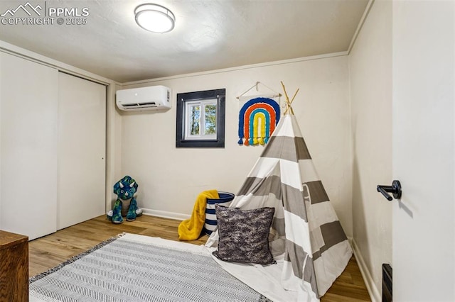 playroom with crown molding, a wall mounted air conditioner, and wood-type flooring