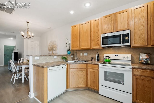 kitchen with hanging light fixtures, sink, white appliances, and light hardwood / wood-style flooring