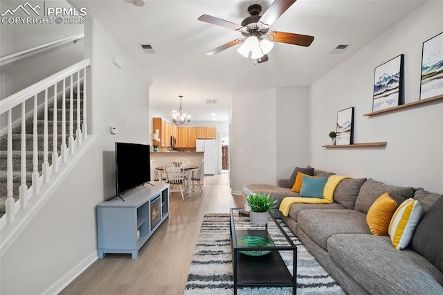 living room with ceiling fan with notable chandelier and light hardwood / wood-style floors