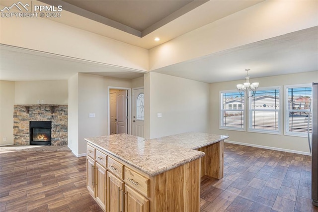 kitchen with baseboards, dark wood-type flooring, a center island, an inviting chandelier, and a stone fireplace