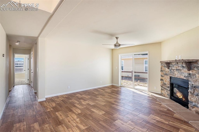 unfurnished living room with a stone fireplace, wood finished floors, a ceiling fan, and baseboards