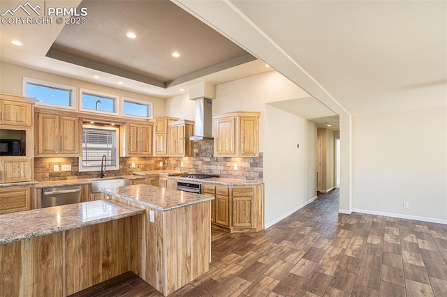 kitchen with dishwasher, wall chimney exhaust hood, light stone counters, a tray ceiling, and a sink