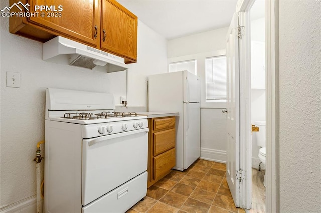 kitchen featuring white appliances, baseboards, brown cabinetry, light countertops, and under cabinet range hood