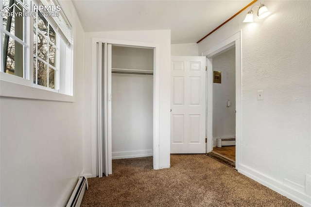 unfurnished bedroom featuring dark colored carpet, a closet, baseboards, and a baseboard radiator