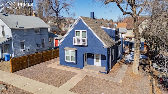 view of front facade featuring a residential view, fence, a balcony, and stucco siding