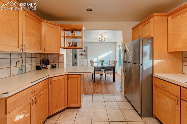 kitchen featuring tasteful backsplash, stainless steel fridge, kitchen peninsula, and light tile patterned floors