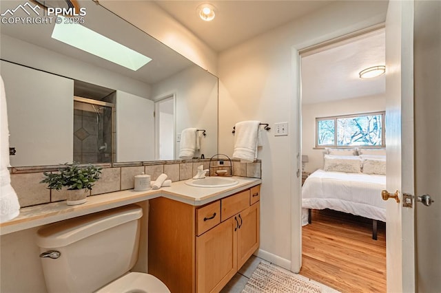 bathroom with a skylight, tasteful backsplash, wood-type flooring, vanity, and toilet