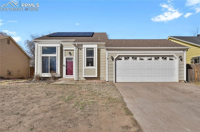 single story home with solar panels, concrete driveway, roof with shingles, an attached garage, and fence