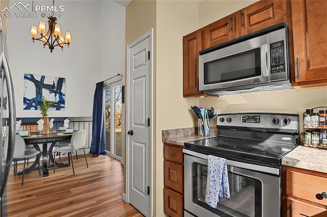 kitchen featuring a chandelier, stainless steel appliances, light wood-style floors, brown cabinetry, and pendant lighting