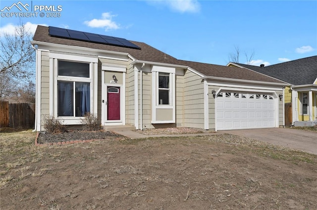 view of front facade featuring solar panels, a shingled roof, concrete driveway, an attached garage, and fence