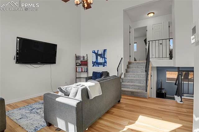 living room with a towering ceiling, ceiling fan, wood finished floors, baseboards, and stairs