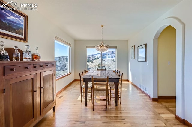 dining area featuring arched walkways, light wood-style flooring, visible vents, and baseboards