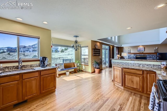 kitchen with brown cabinets, light wood finished floors, visible vents, a sink, and range with electric cooktop