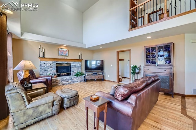 living area featuring visible vents, baseboards, a towering ceiling, wood finished floors, and a stone fireplace