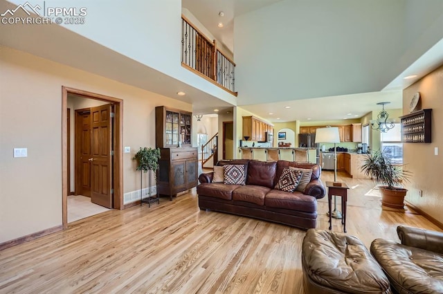 living room with light wood-style floors, a chandelier, baseboards, and stairs