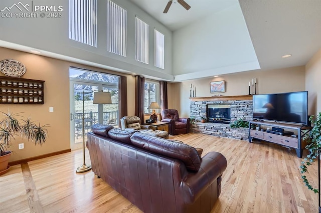 living area with light wood-type flooring, a fireplace, baseboards, and a towering ceiling