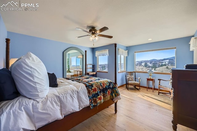 bedroom with a ceiling fan, multiple windows, baseboards, and wood finished floors