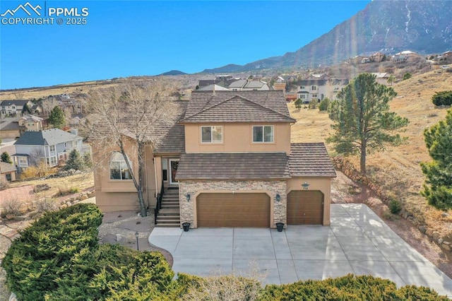 view of front facade featuring stone siding, a mountain view, concrete driveway, and stucco siding