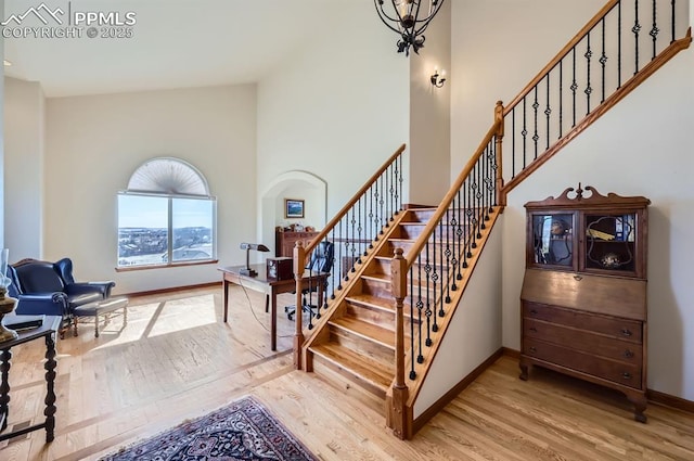 stairway with a towering ceiling, baseboards, and wood finished floors