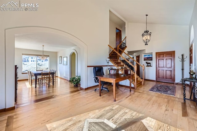 entryway featuring arched walkways, wood finished floors, a towering ceiling, stairs, and an inviting chandelier