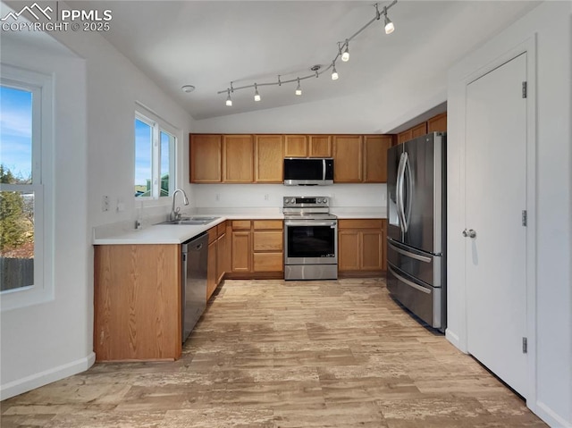 kitchen featuring sink, appliances with stainless steel finishes, track lighting, vaulted ceiling, and light wood-type flooring