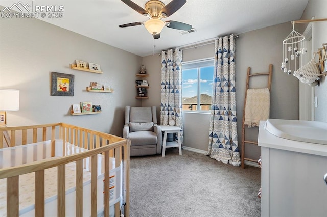 carpeted bedroom with a nursery area, sink, and ceiling fan