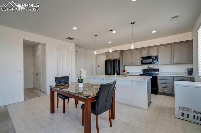 kitchen with gray cabinetry, decorative light fixtures, a center island with sink, and black appliances